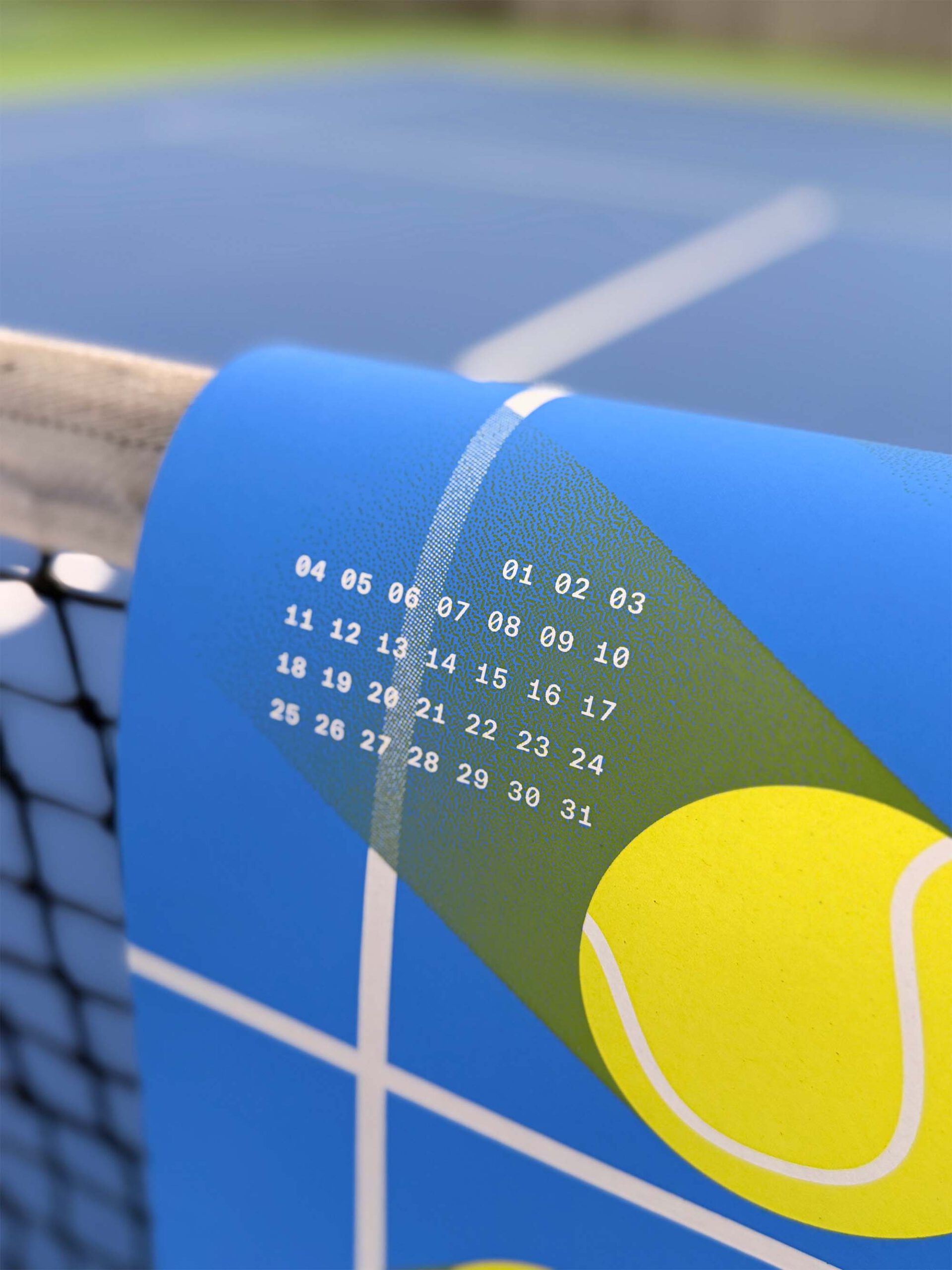Close-up of the studio_upstruct calendar draped over a tennis net on a blue tennis court, showing the calendar grid.